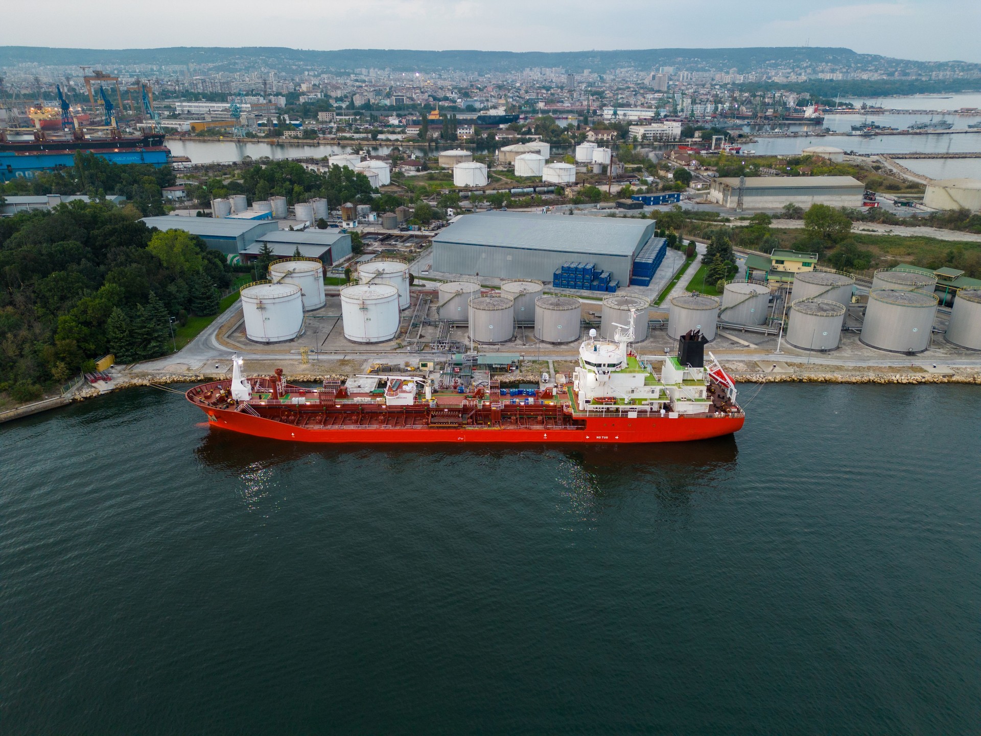 Tanker ship refueling at an oil terminal with storage silo's in the port, aerial view